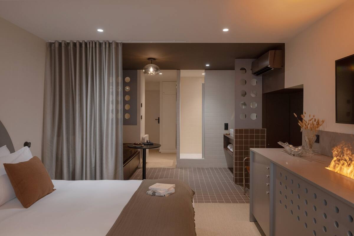 A hotel room with a bed, a desk, a mirror, and a bathroom visible through an open door.