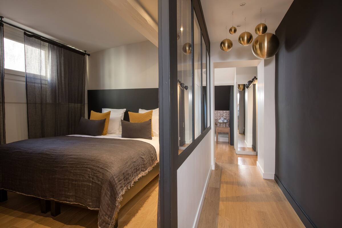 A modern bedroom with a large bed, a dark headboard, and a view of a hallway with a staircase.