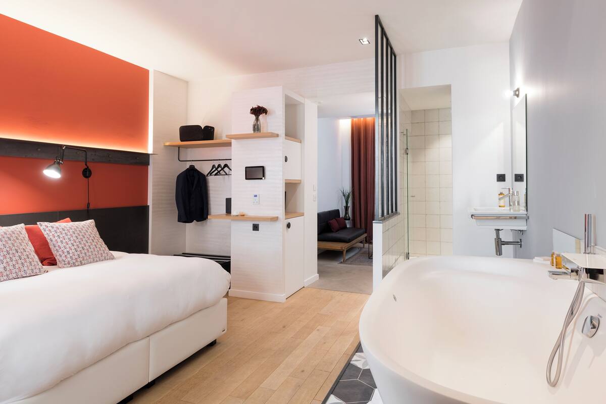 A modern hotel room with a large bed, a separate bathroom with a bathtub, and a walk-in closet.