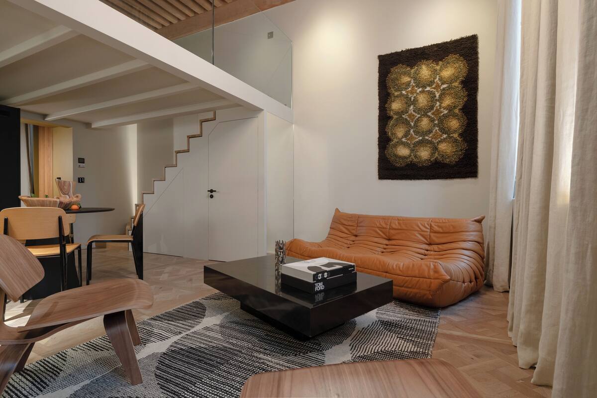 A modern living room with a glass coffee table, leather sofa, and a staircase leading to an upper level.
