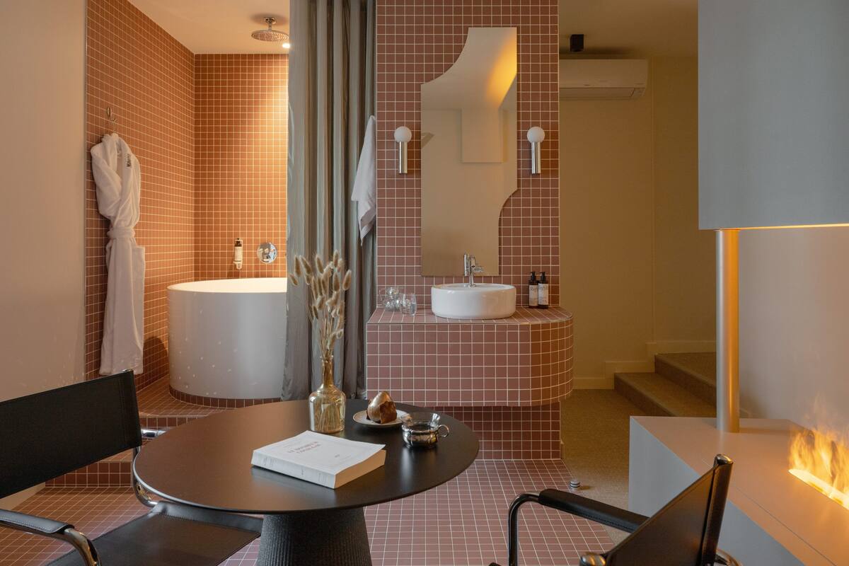 A modern bathroom with a bathtub, sink, and mirror. There is a table with a book and a vase.
