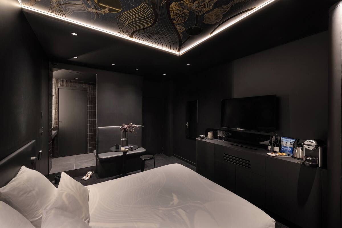 A modern hotel room with a bed, a desk, a TV, and a minibar.