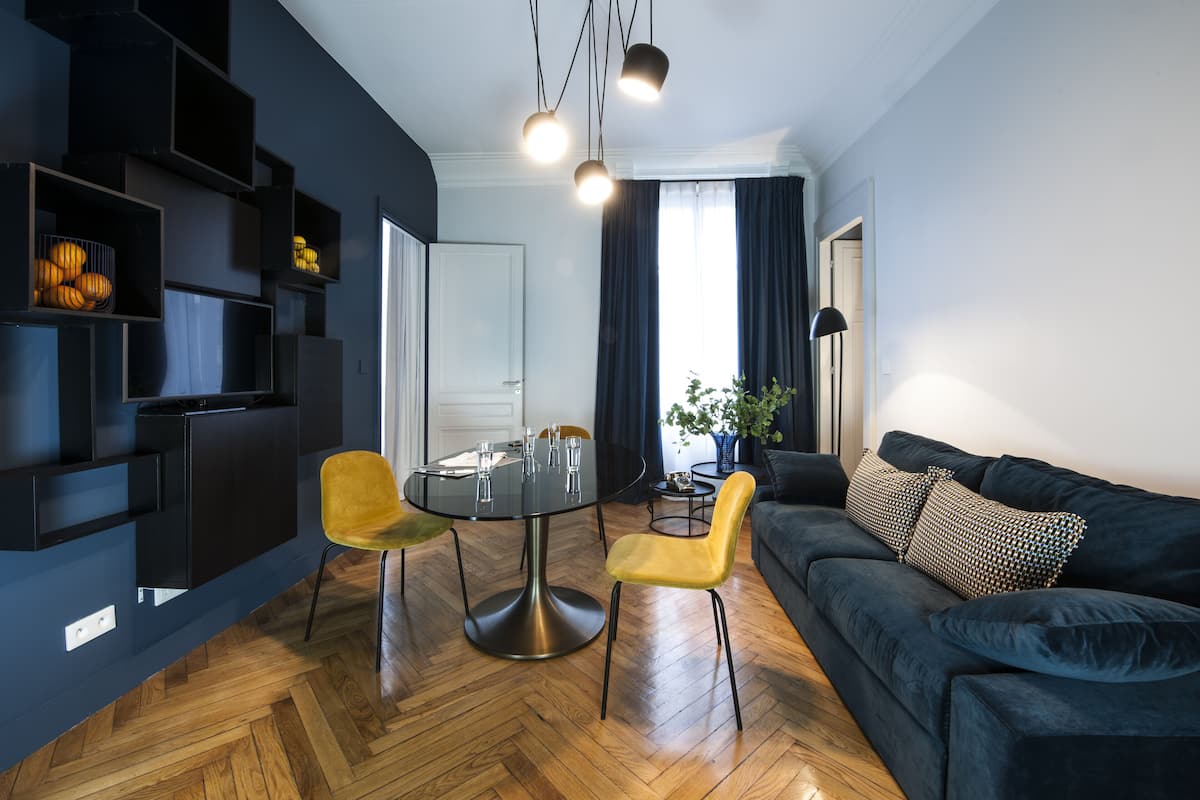 A modern living room with a dark blue sofa, yellow chairs, a round dining table, and built-in black shelving.