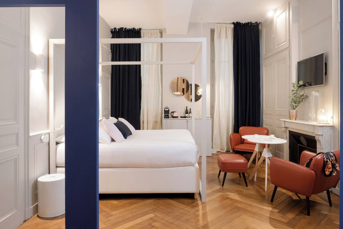 A modern hotel room with a white bed, a small round table, and two red chairs.