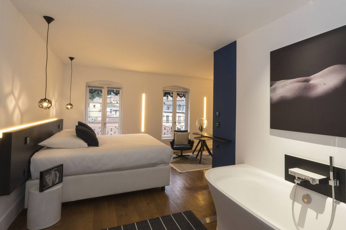 A modern bedroom with a bed, bedside table, and a large window.