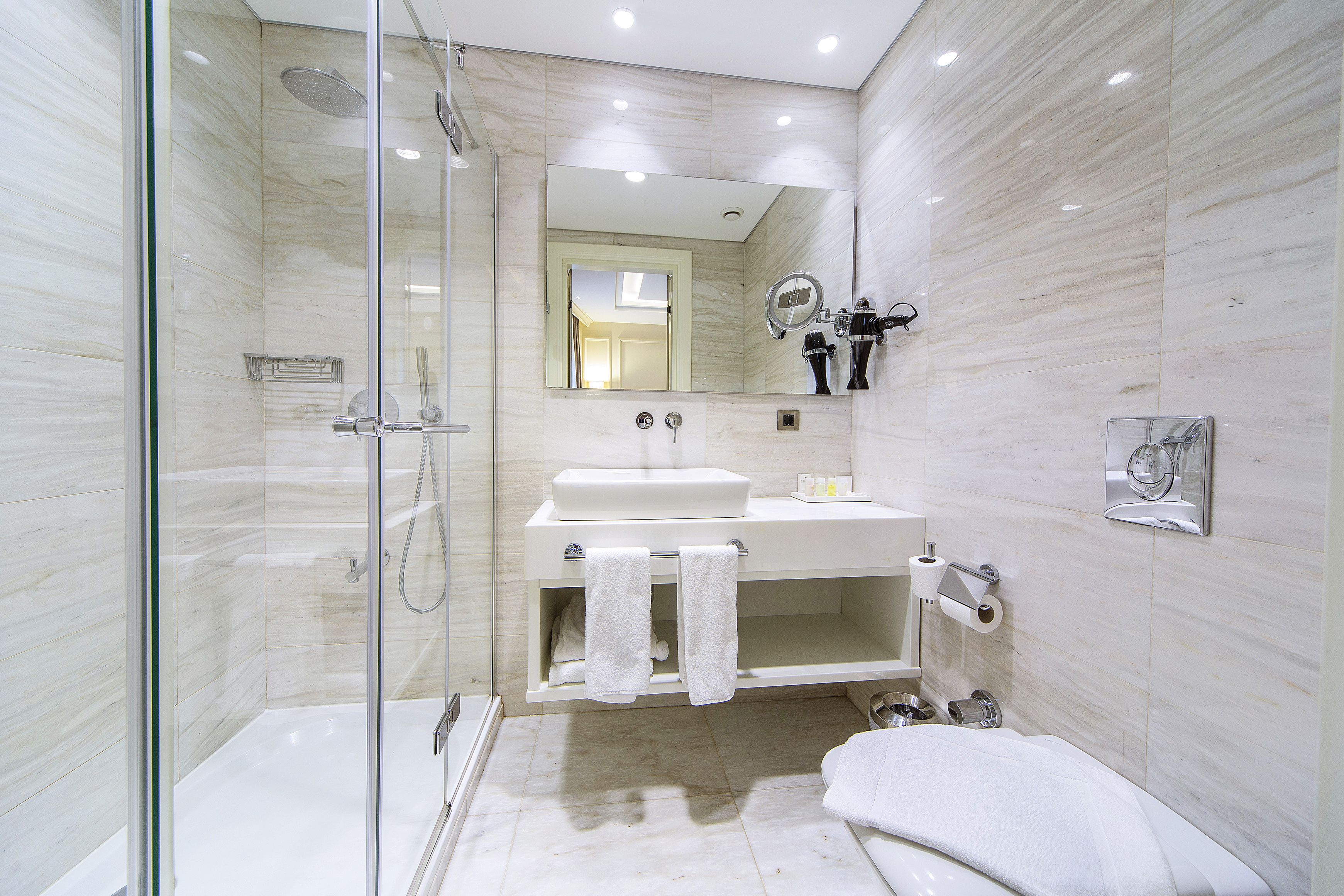 Un baño moderno con cabina de ducha de vidrio, un lavamanos blanco y un espejo grande.