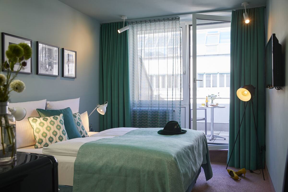A hotel room with a bed, a desk, a chair, a lamp, a TV, and a window with curtains.