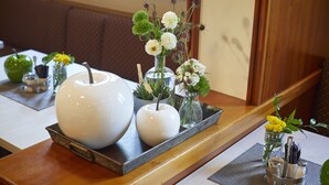 A dining table with a tray holding a large white bowl, a smaller white bowl, and a glass vase with flowers. - Hotel Metropol by Maier Privathotels (Munich)
