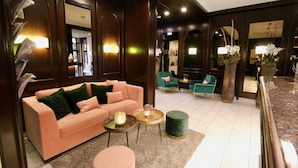 A lobby with a pink sofa, green chairs, and a marble reception desk. - Hotel Metropol by Maier Privathotels (Munich)