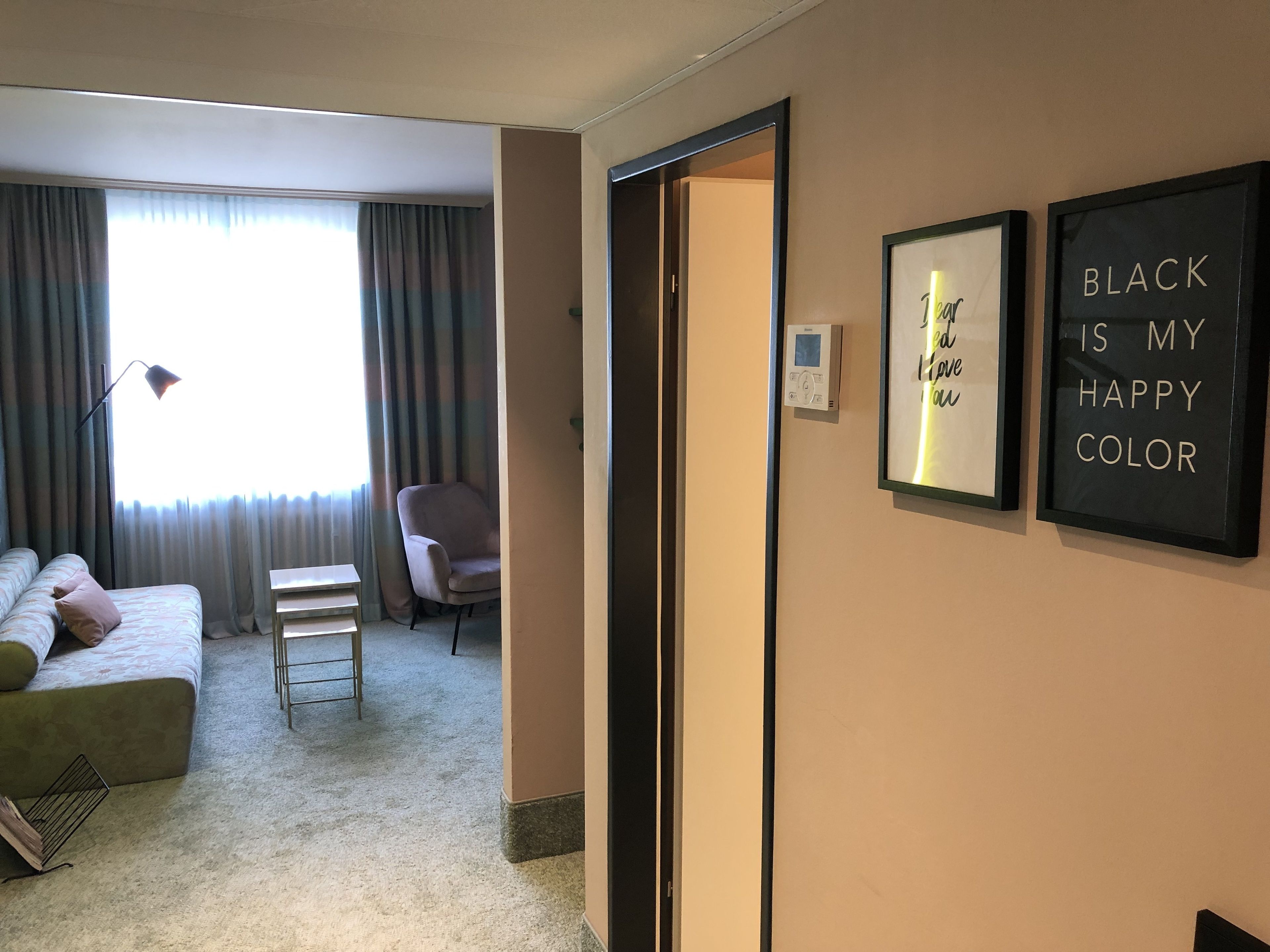 A hotel room with a bed, a chair, a small table, and a wall with framed inspirational quotes.
