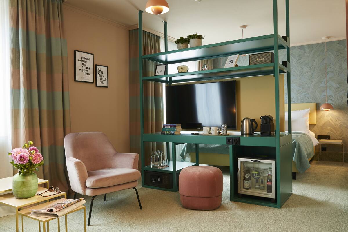 A hotel room with a bed, a desk with a TV, a chair, a small fridge, and a coffee maker.