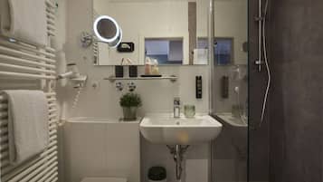 Une salle de bain moderne avec un lavabo blanc, une douche à parois de verre, un miroir doté d’un anneau lumineux et un porte-serviettes.