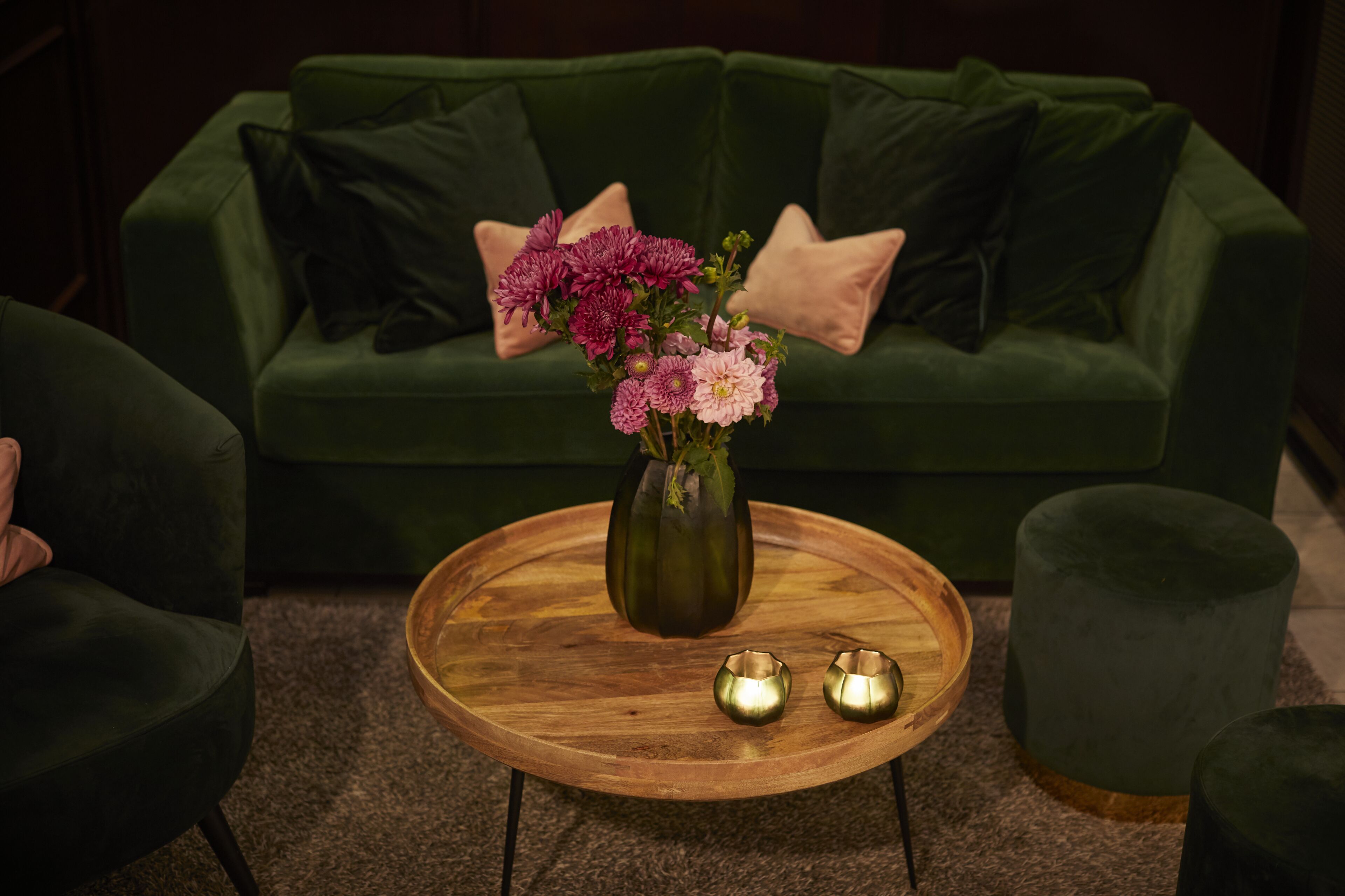Un canapé vert, un vase de fleurs et deux chandeliers posés sur une table en bois.
