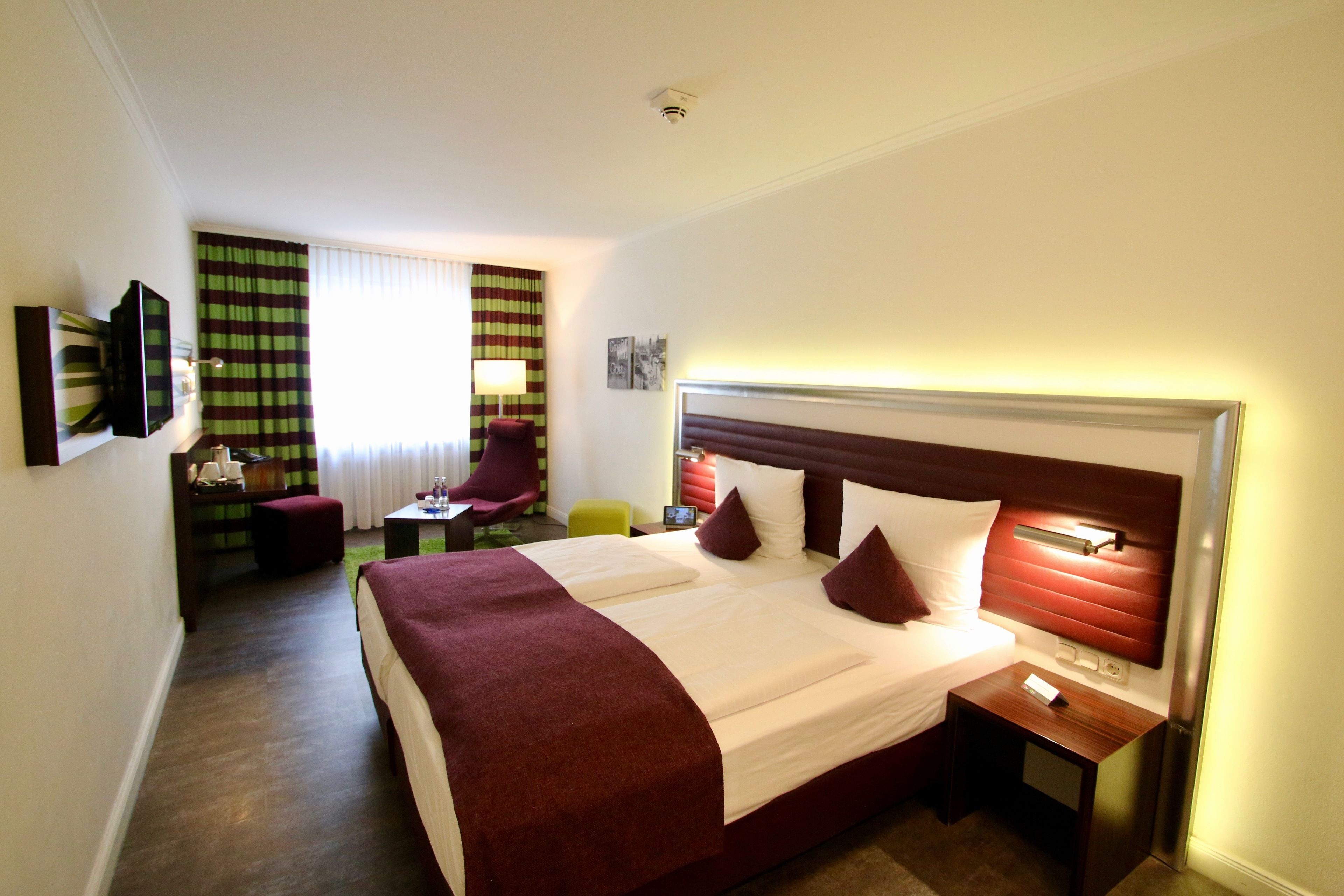 Habitación de hotel con una cama grande, un escritorio con una silla, un televisor y una ventana con cortinas.