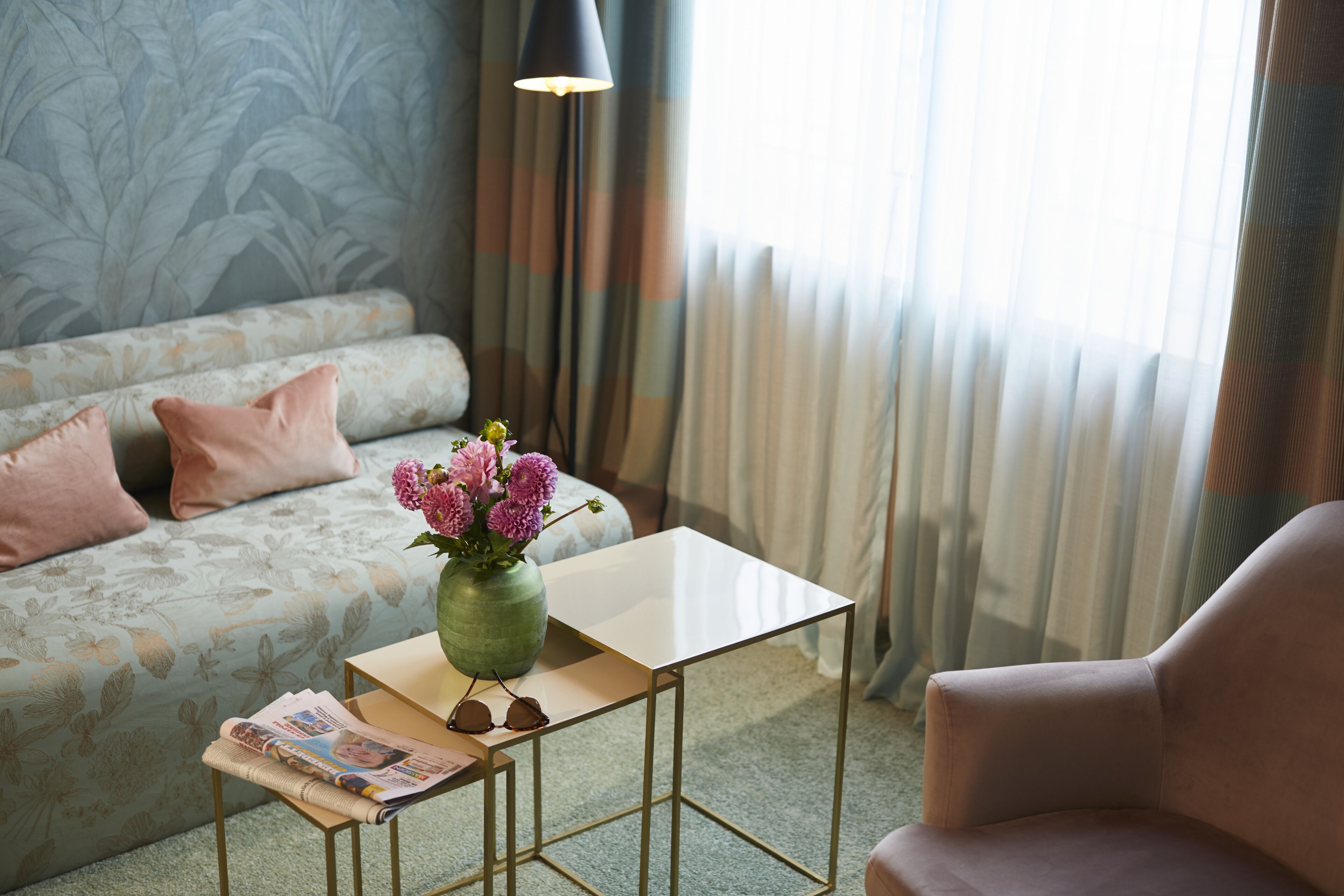 A room with a sofa, a small table with a vase of flowers, and a lamp.