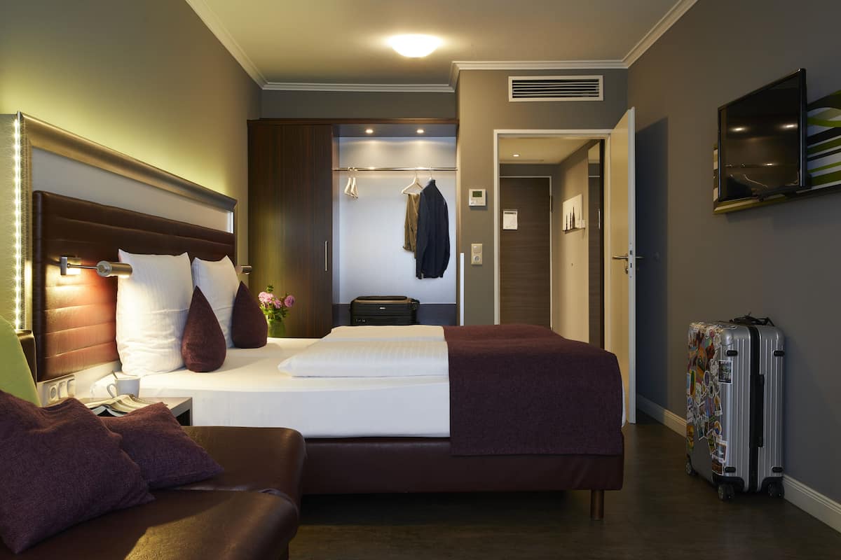 A hotel room with a large bed, a bedside table, a wardrobe, a mirror, and a suitcase.