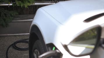 Ein weißes Auto, das an einer elektrischen Ladestation angeschlossen ist.