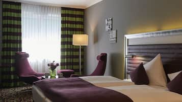 Een hotelkamer met een groot bed, twee stoelen, een klein tafeltje met een vaas en een lamp.