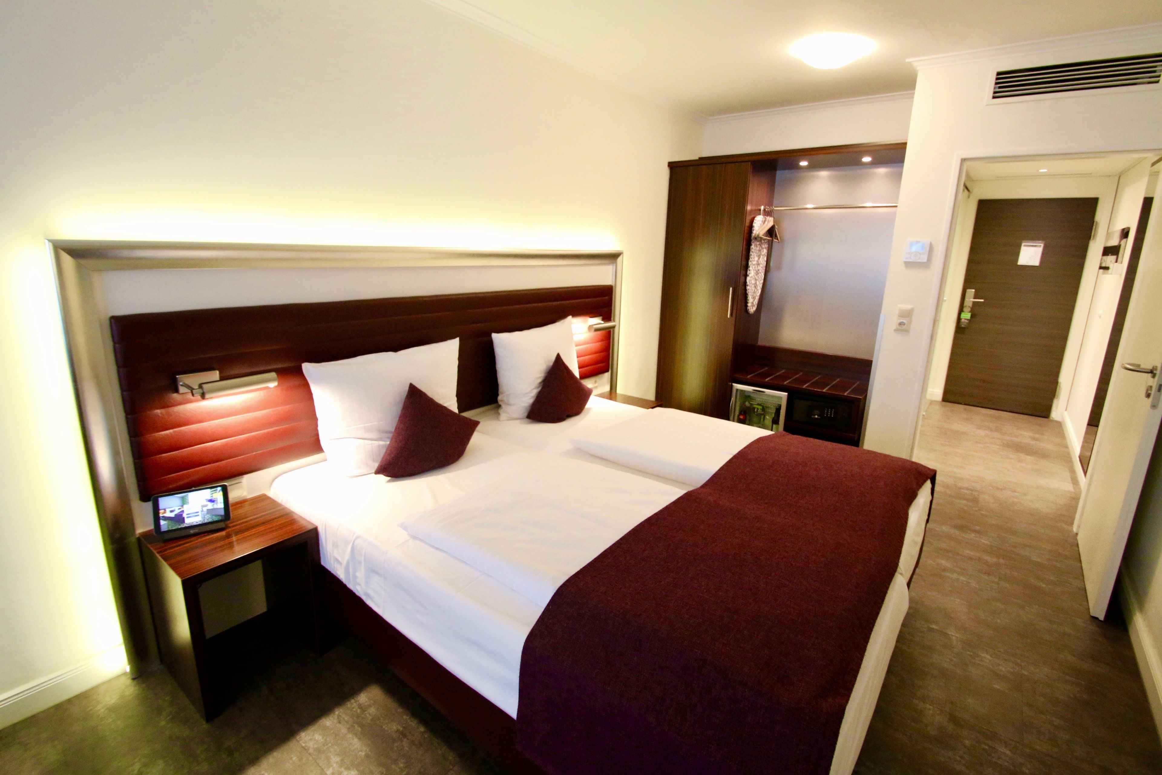 A hotel room with a large bed, a bedside table with a lamp, and a wardrobe.
