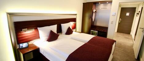A hotel room with a large bed, a bedside table with a lamp, and a wardrobe.