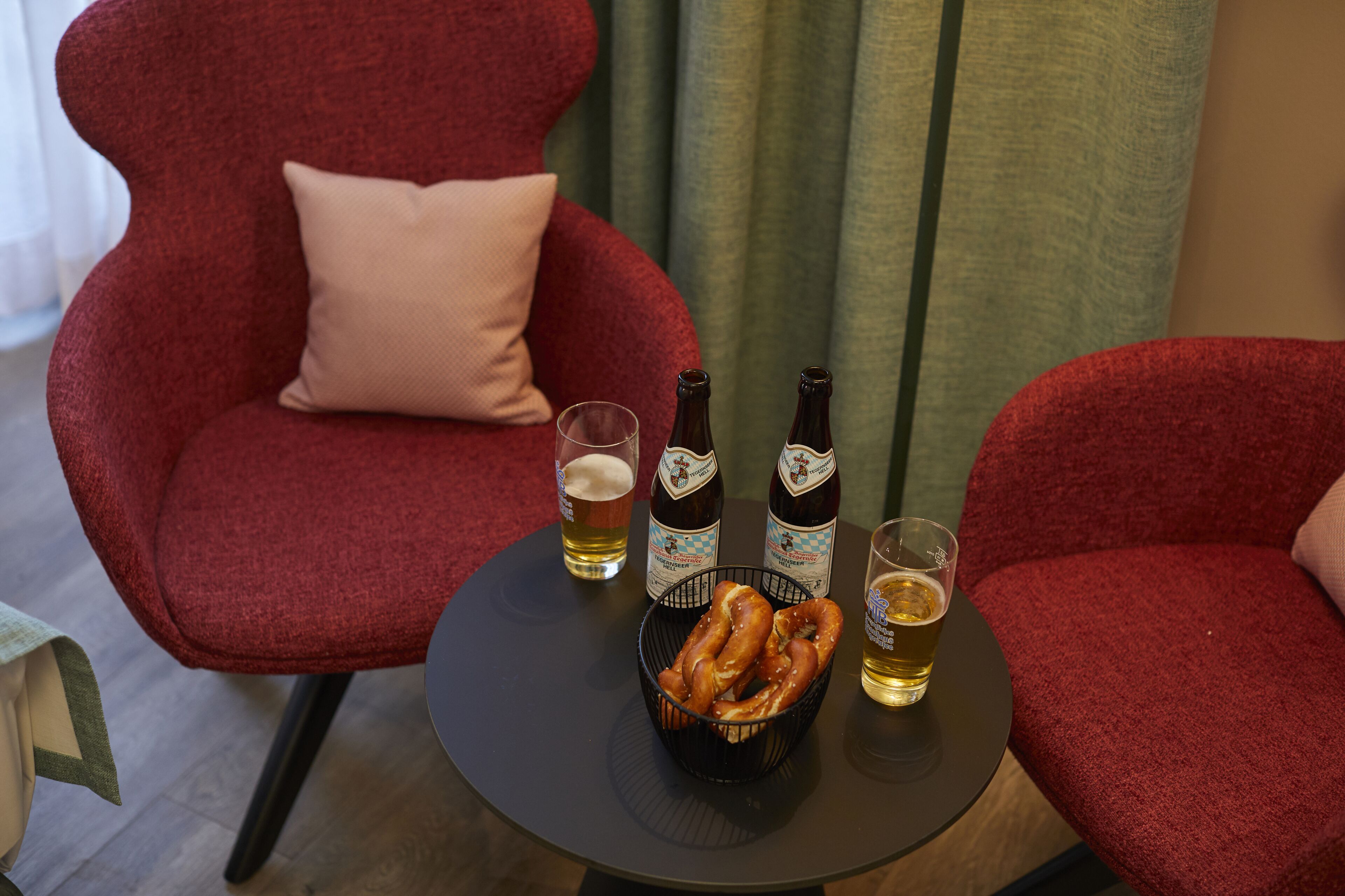A table with two bottles of beer, a glass of beer, and a basket of pretzels.