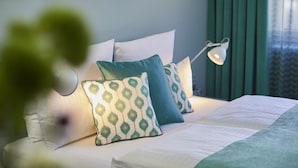 A neatly made bed with patterned pillows and a bedside lamp, set against a green wall with framed pictures. - Hotel Metropol by Maier Privathotels (Munich)
