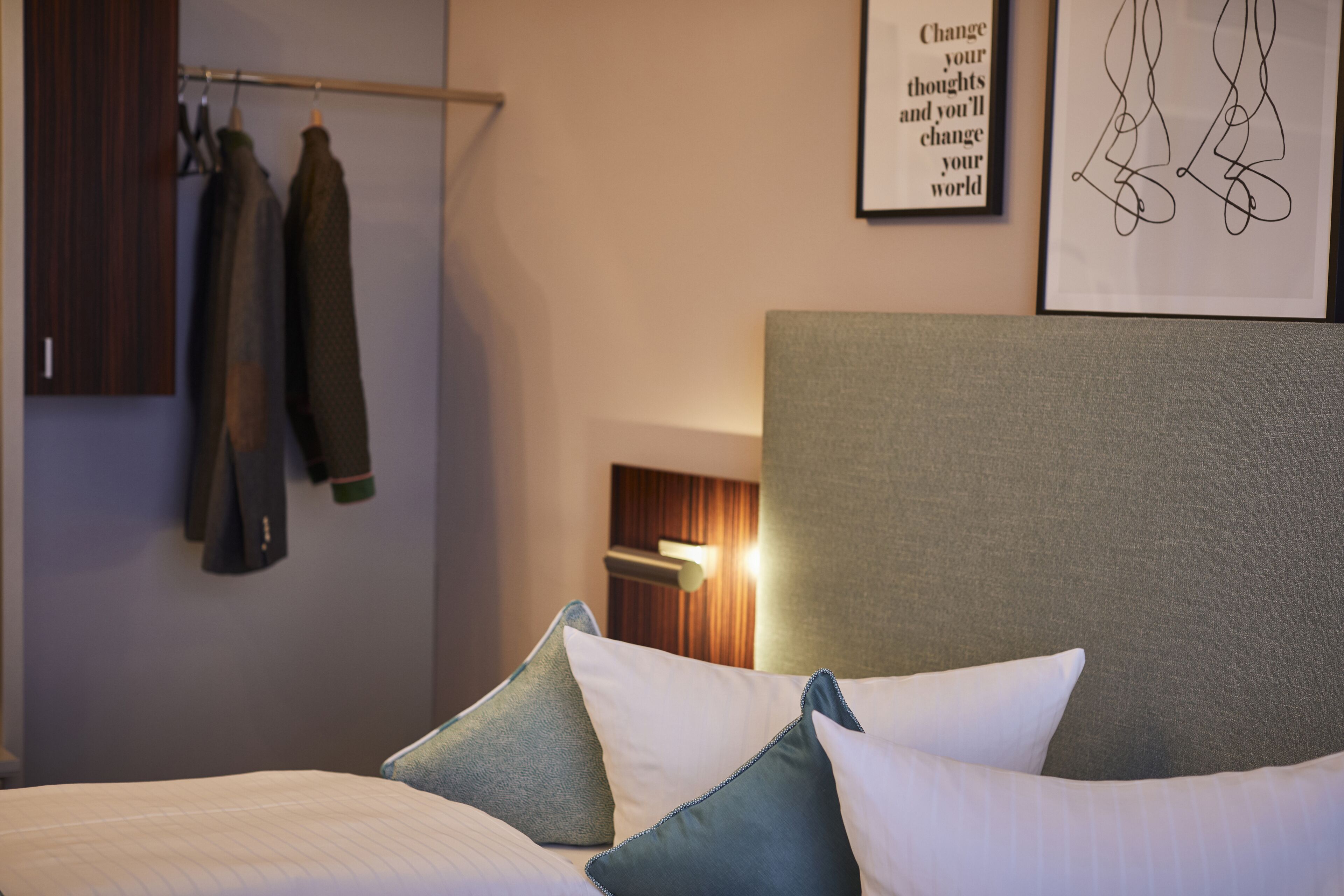 Una cama bien tendida con almohadas, un armario de madera y una cita inspiradora enmarcada en la pared.