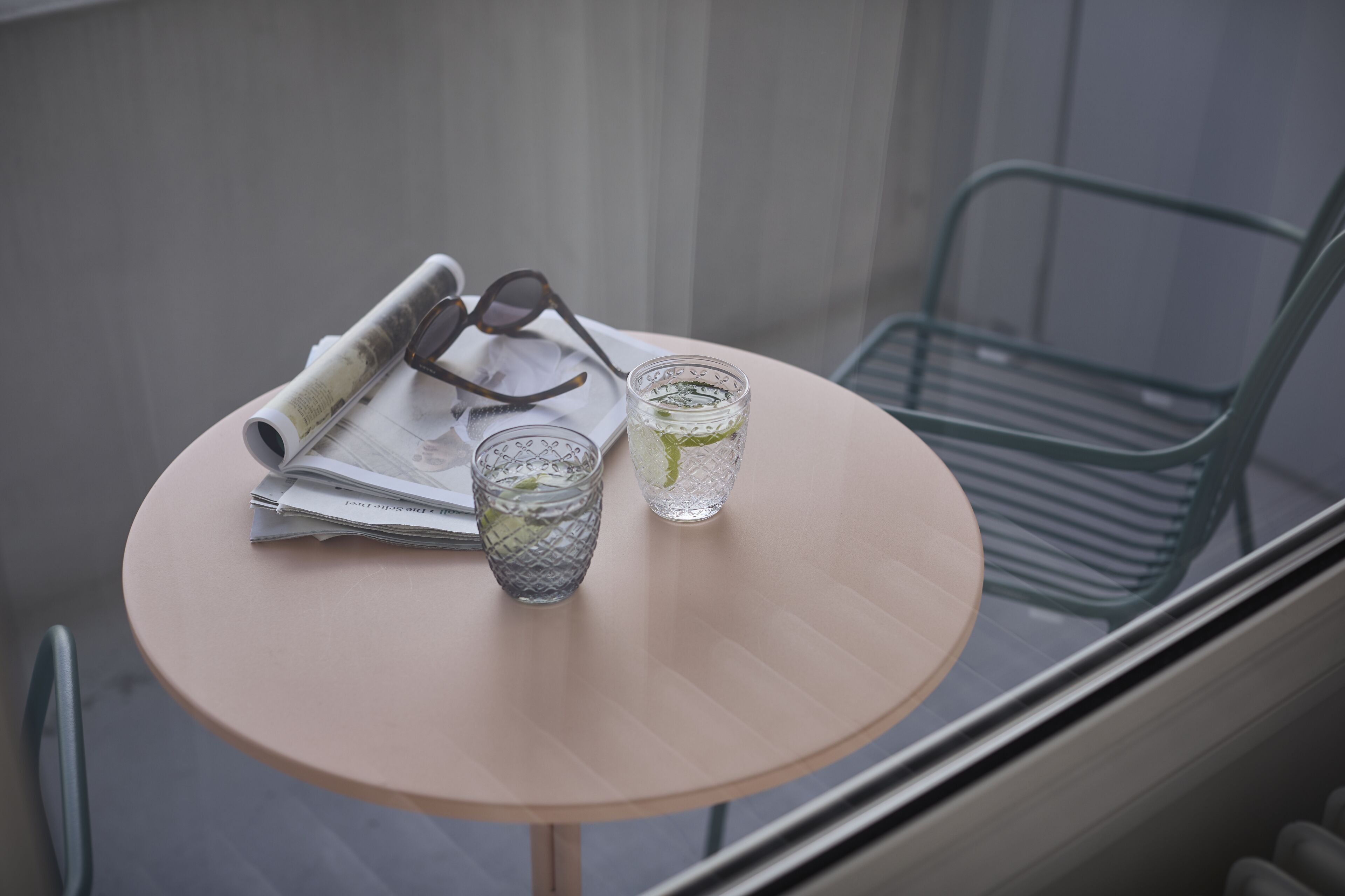 Un tavolo rotondo con un giornale, bicchieri e due bicchieri d'acqua e lime.