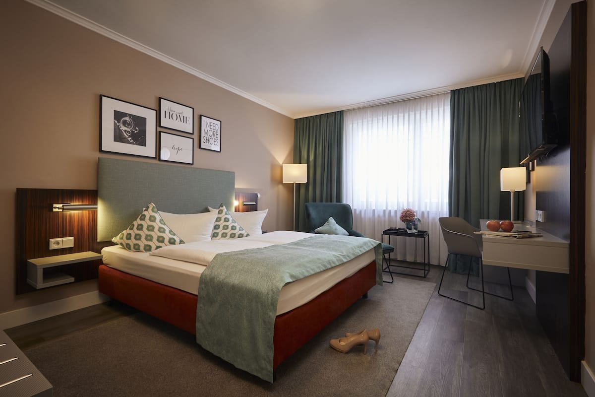 A hotel room with a bed, desk, chair, and a TV.