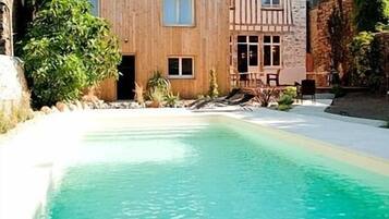 Una piscina con agua cristalina, rodeada por una cubierta de madera y muros de piedra.