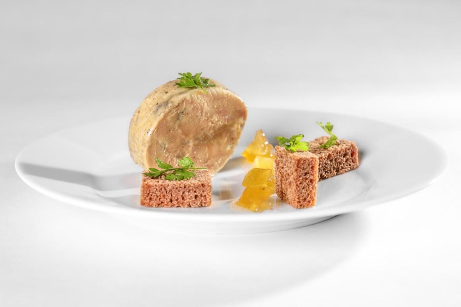A white plate with a large piece of pâté, two small pâté cubes, and a lemon slice.