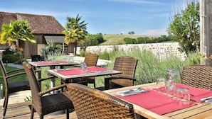 An outdoor dining area with wicker chairs and tables, a stone wall, and a view of the countryside.