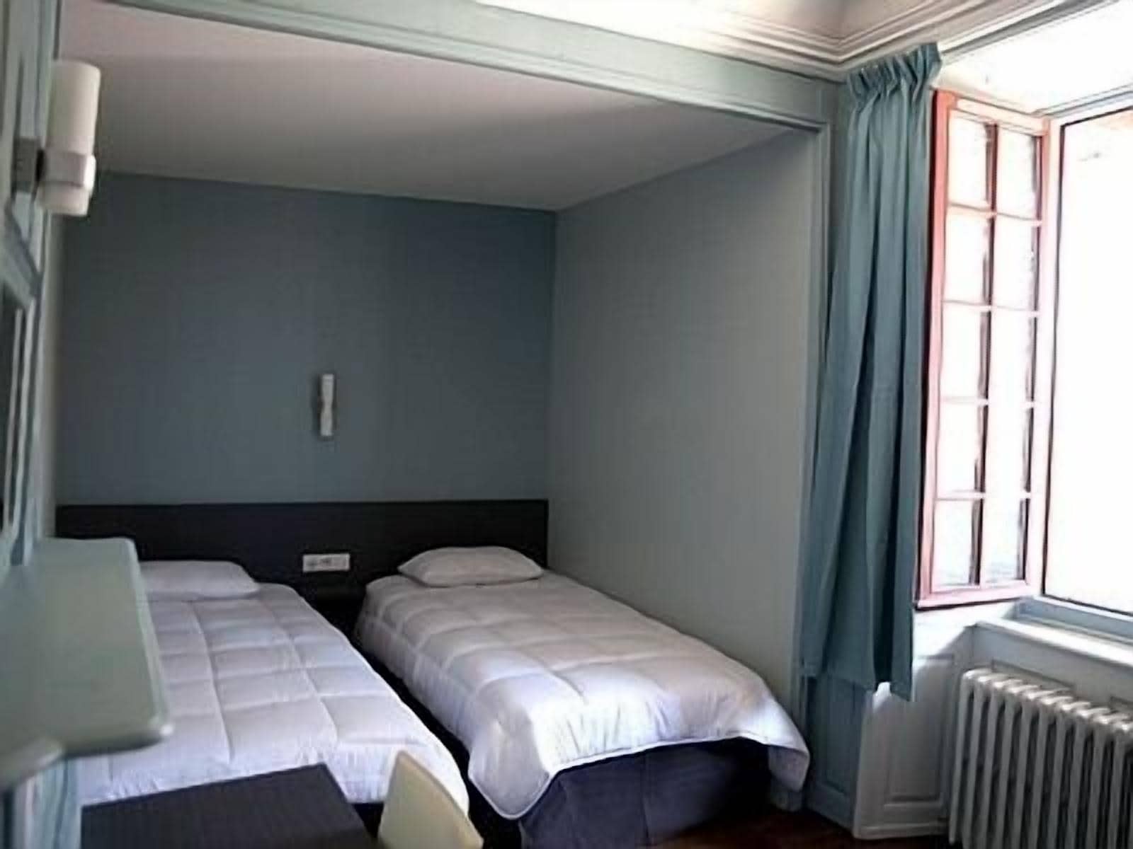 A room with two single beds, a small table, and a window with curtains.