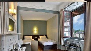 A hotel room with a bed, bedside table, and a view of the outside.