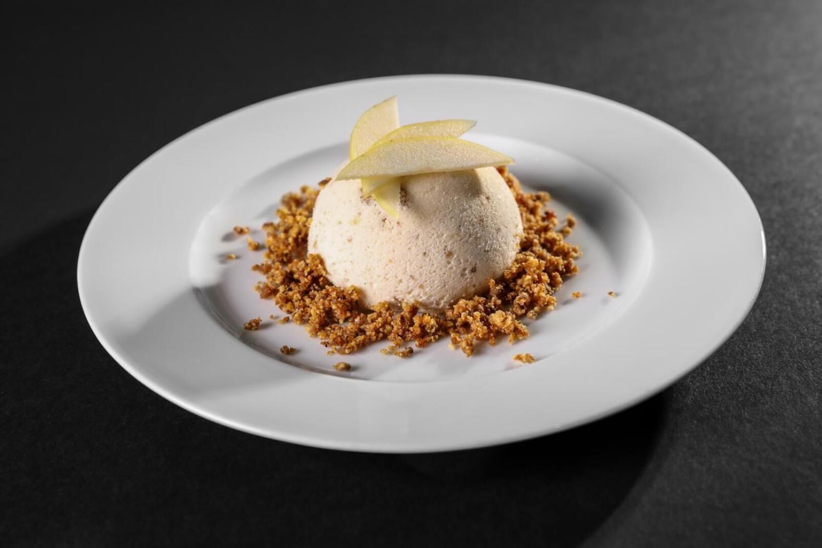 A dessert on a white plate with crumbled topping and a pear slice on top.