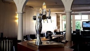 A bar area with a decorative metal sculpture, white columns, and a long counter with bar stools.
