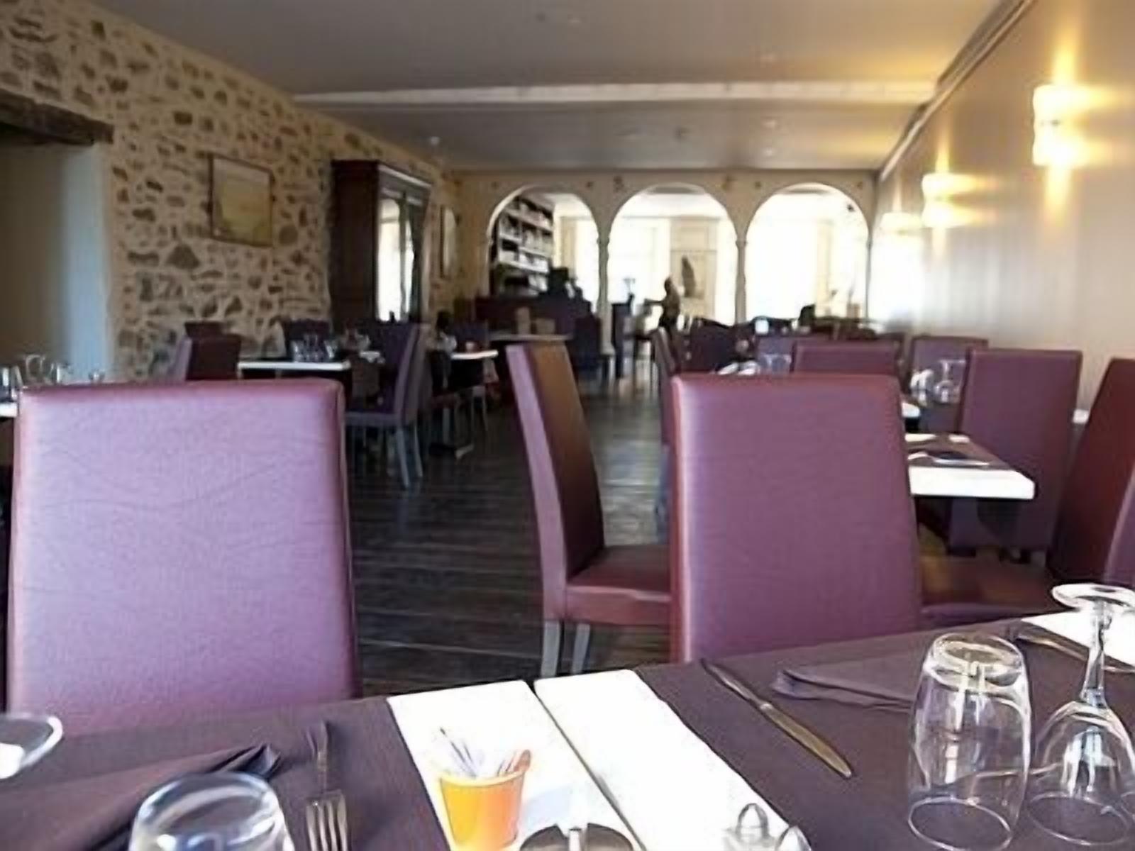 Interior de restaurante com paredes de pedra, cadeiras estofadas em roxo e mesas preparadas para refeições.