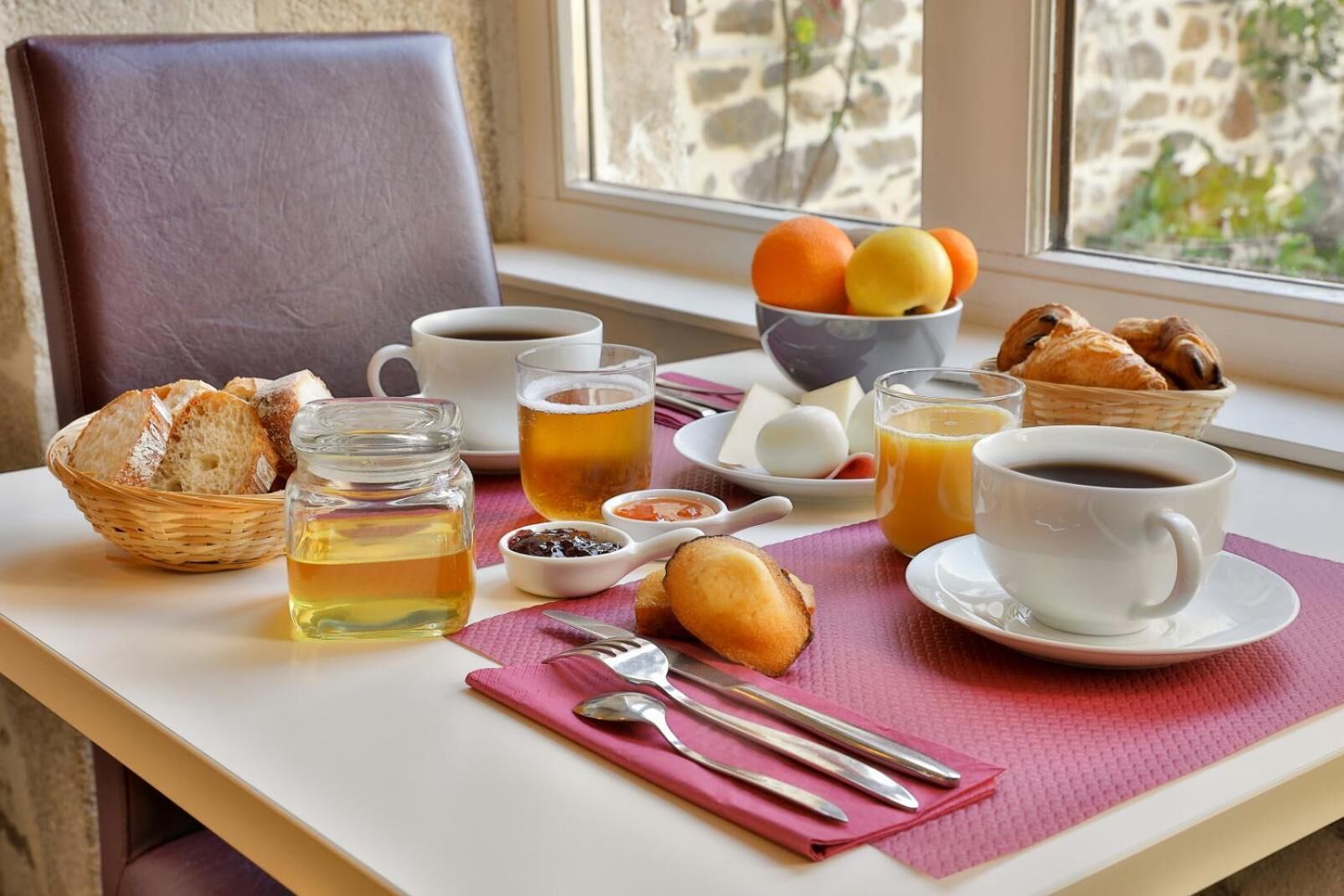 Una mesa de desayuno con pan, bollería, frutas, té, café y salsas.