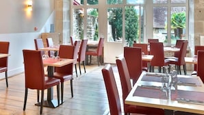 A restaurant with red chairs and tables, large windows, and a view of the outdoors.