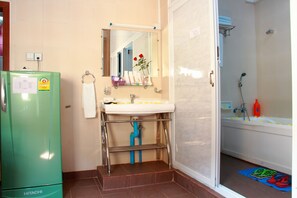 Une salle de bain avec un réfrigérateur vert, un lavabo avec un miroir et un espace douche.