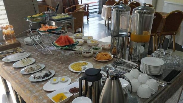 A buffet setup with various food items and beverages, including fruits, salads, and hot dishes, arranged on a table with serving utensils and cups. - MK Hotel (Yangon)