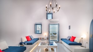 A modern living room with two sofas, a coffee table, and a chandelier. - Fava Eco Suites (Santorini)