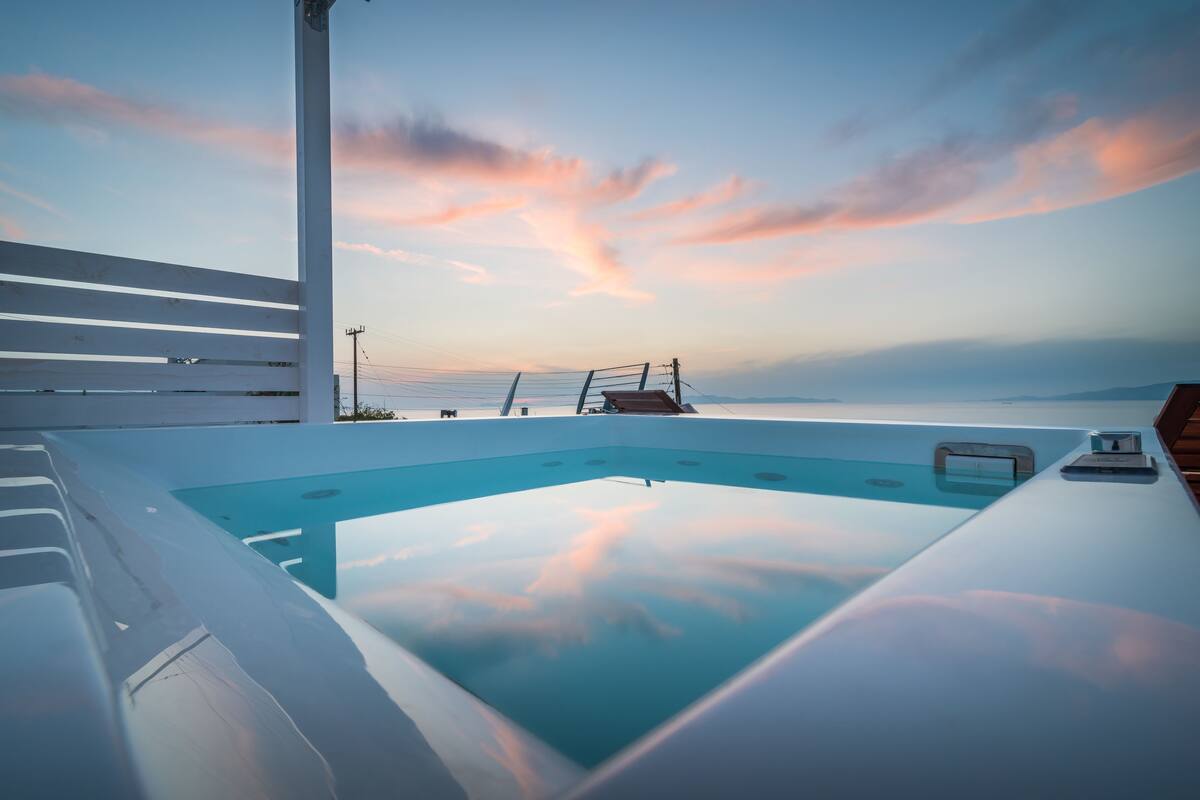 A modern outdoor hot tub with a clear view of the ocean and a sunset sky.