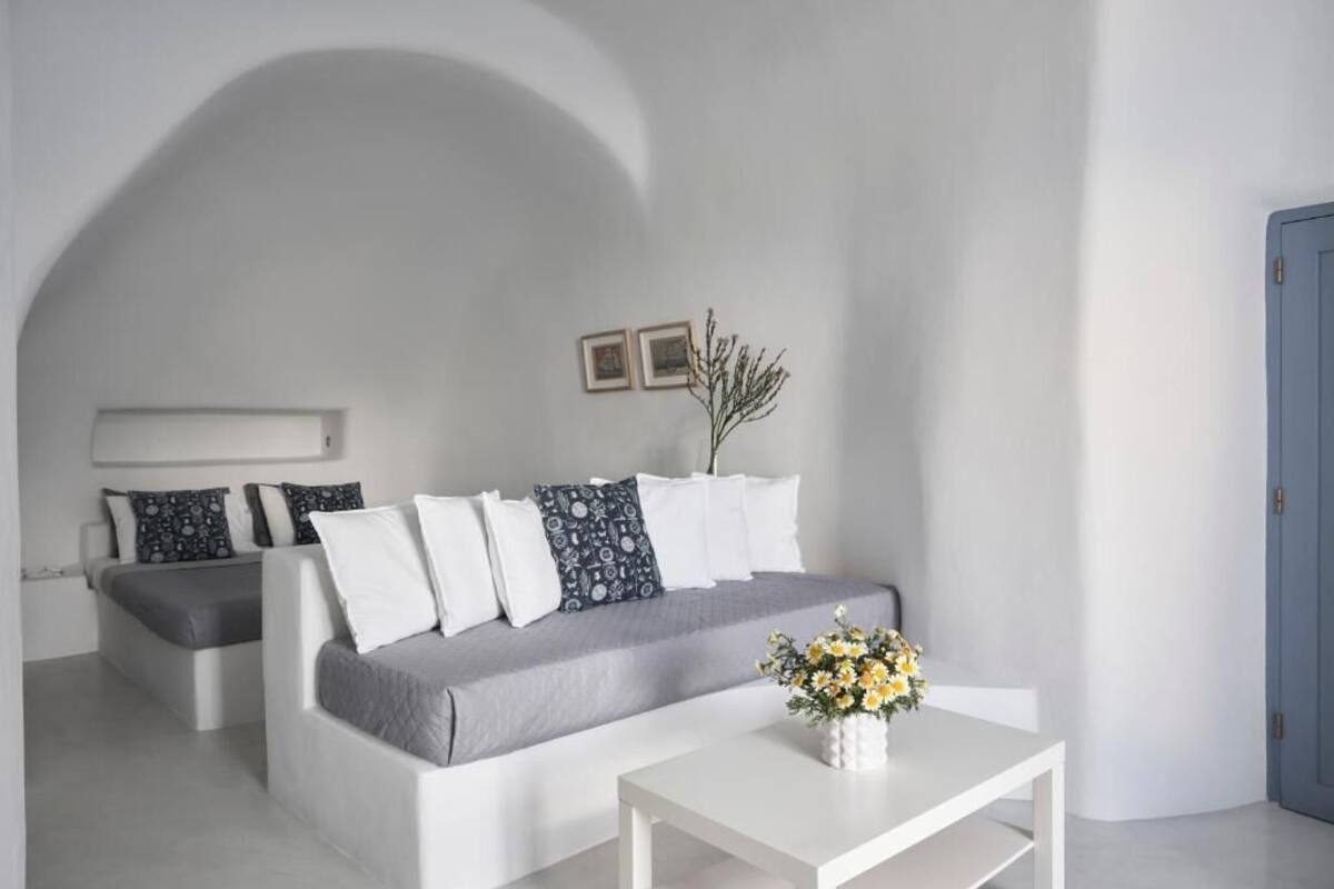 A modern, minimalist room with a white sofa, a small white table with a vase of flowers, and a blue door.