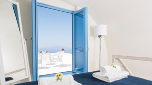 A hotel room with a bed, a nightstand, a lamp, and a view of the sea through an open door. - Fava Eco Suites (Santorini)