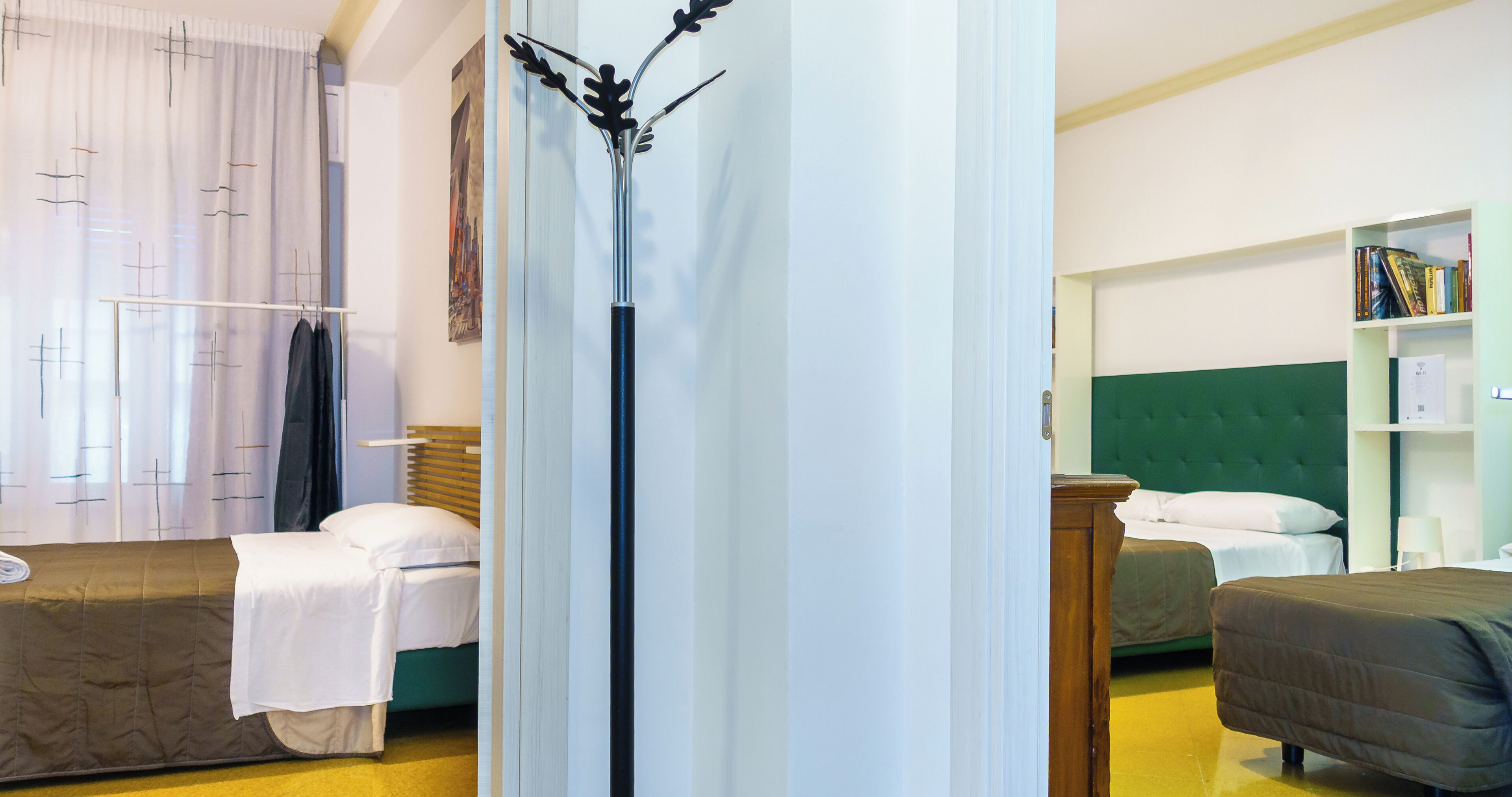 A hotel room with two beds, a wardrobe, a bookshelf, and a decorative floor lamp.