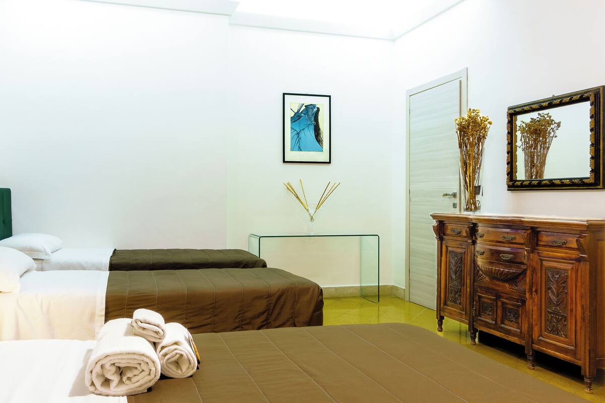 A hotel room with two beds, a wooden dresser, a glass side table, and a framed picture on the wall.
