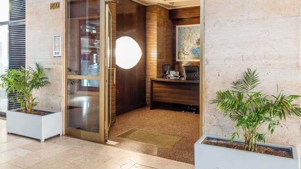 A reception area with a glass door, a desk with a computer, and two potted plants. - Suiteincenter Apartments (Palermo)