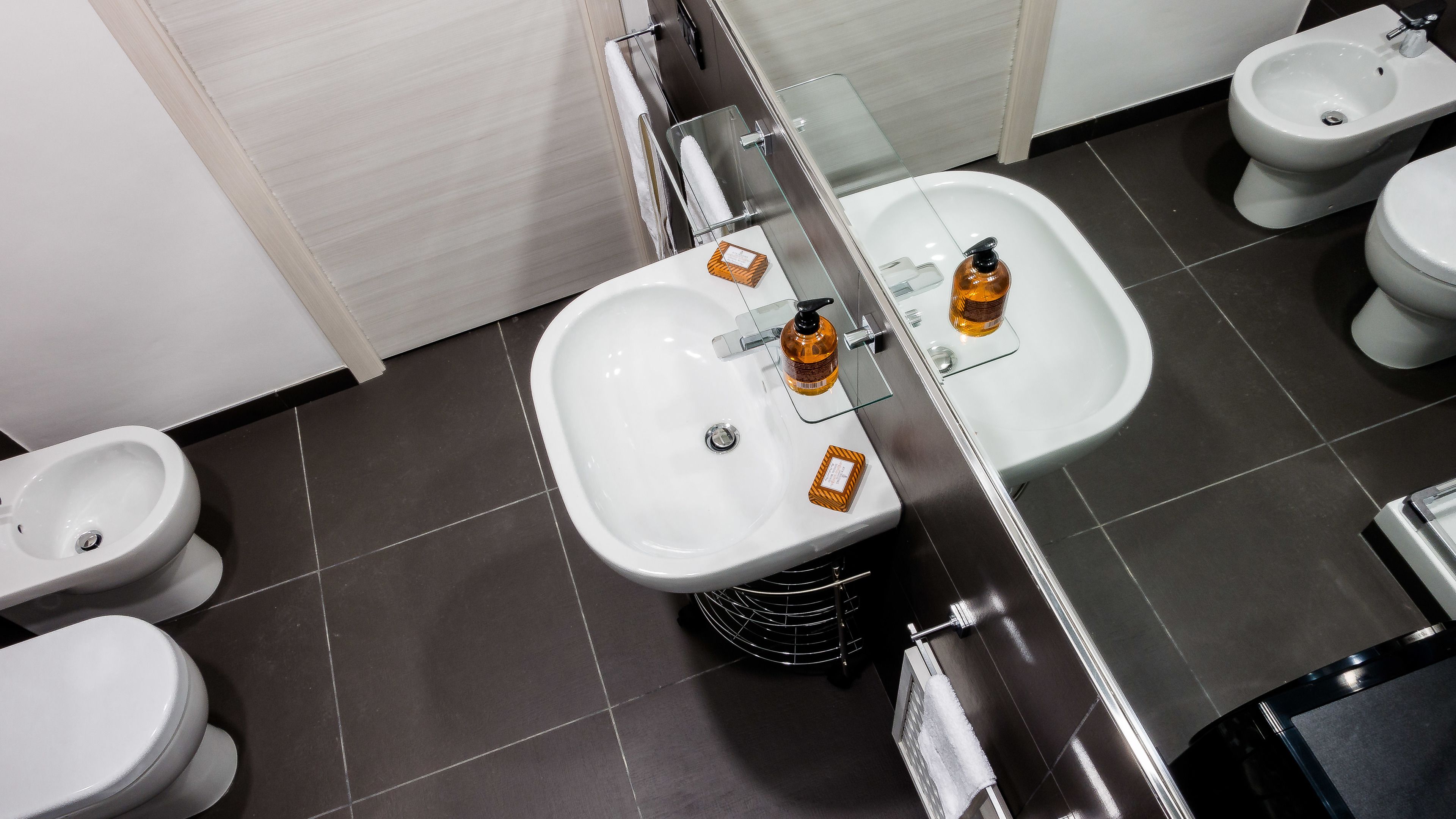A modern bathroom with a white sink, two urinals, and a bidet.