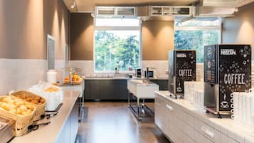 Eine moderne Kaffeestation mit markierten Spendern, ein Frühstücksbereich mit Gebäck und Blick ins Grüne.